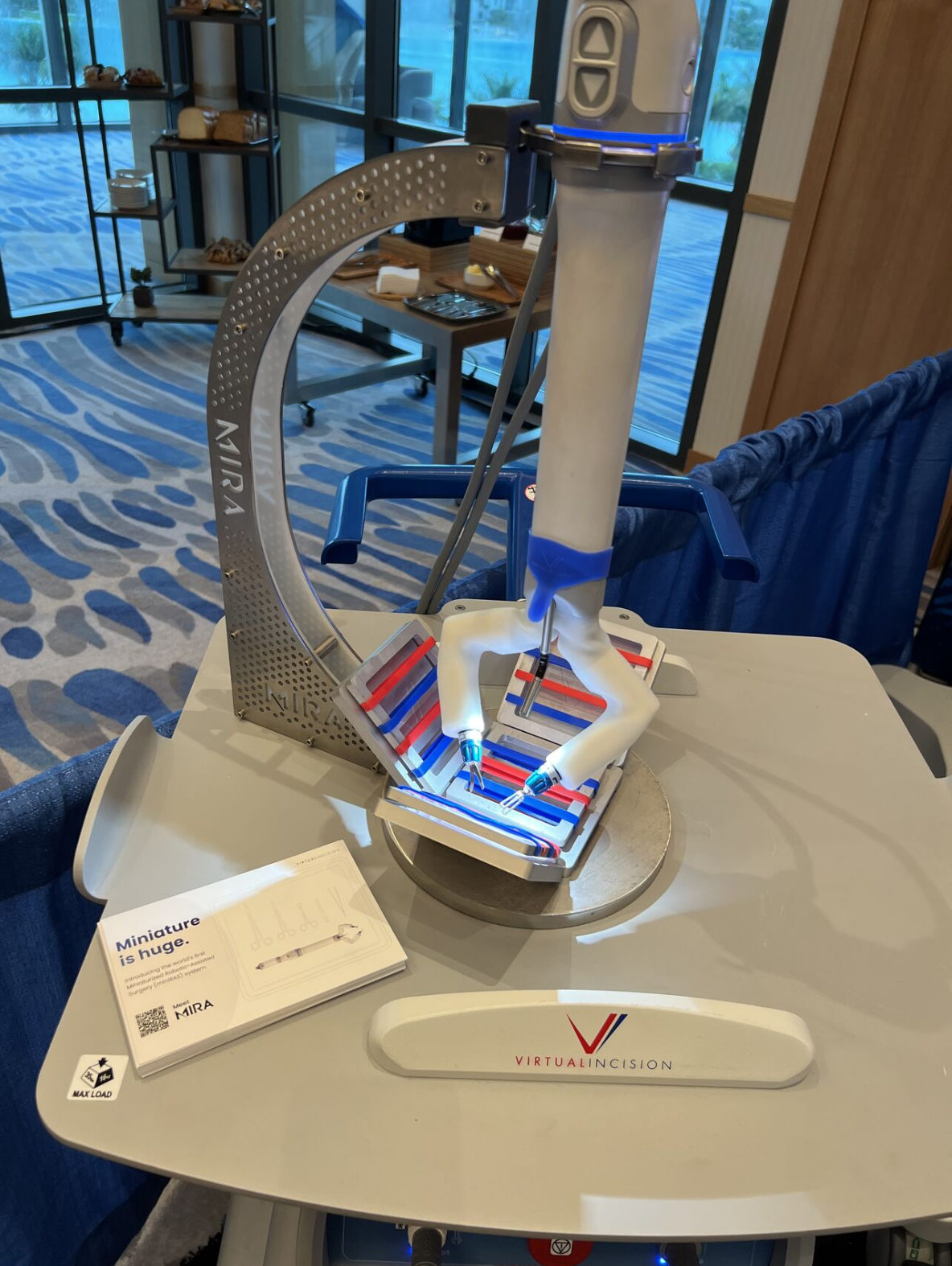 MIRA demo unit on a cart at a surgical conference with a Miniature is huge brochure